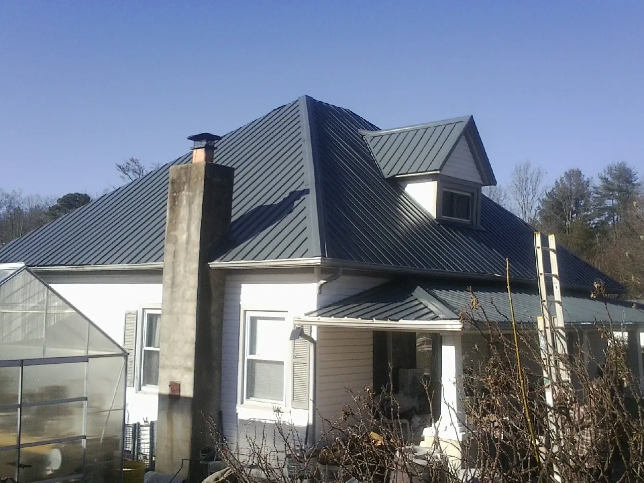 Dark blue standing seam metal roof on a white farmhouse with dormer — Slate & Tile Roof Repair by Roofing Brothers in Edwards