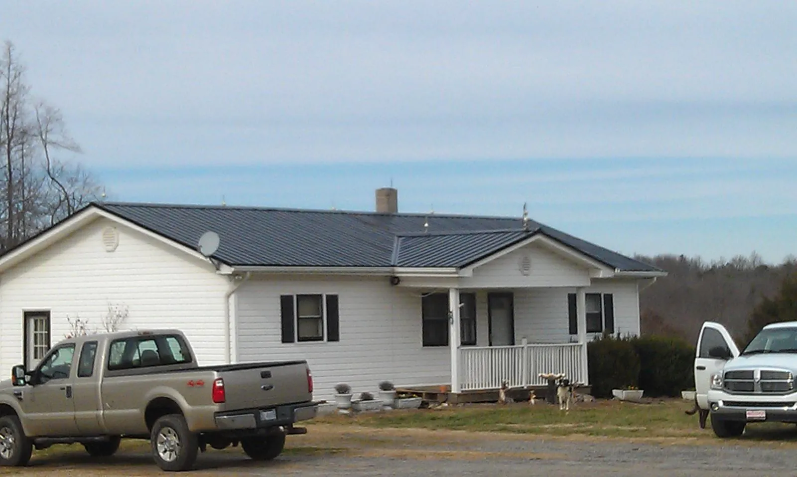 Finished dark metal roof on a white ranch home with work trucks parked in Edwards