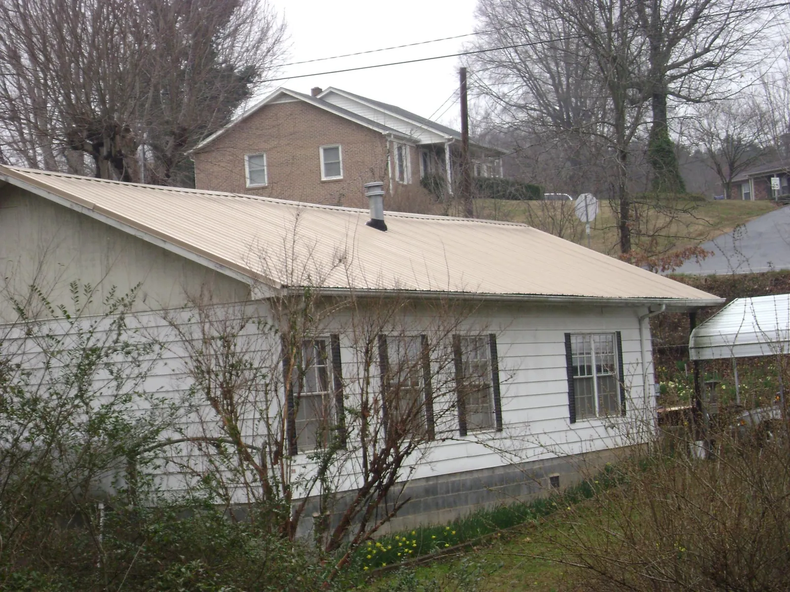 Tan metal roof on a white sided house set into a hillside — Commercial Roofing by Roofing Brothers in Edwards